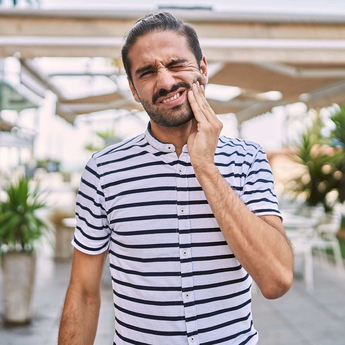 Young hispanic man with beard outdoors at the city touching mouth with hand with painful expression because of toothache or dental illness on teeth. dentist