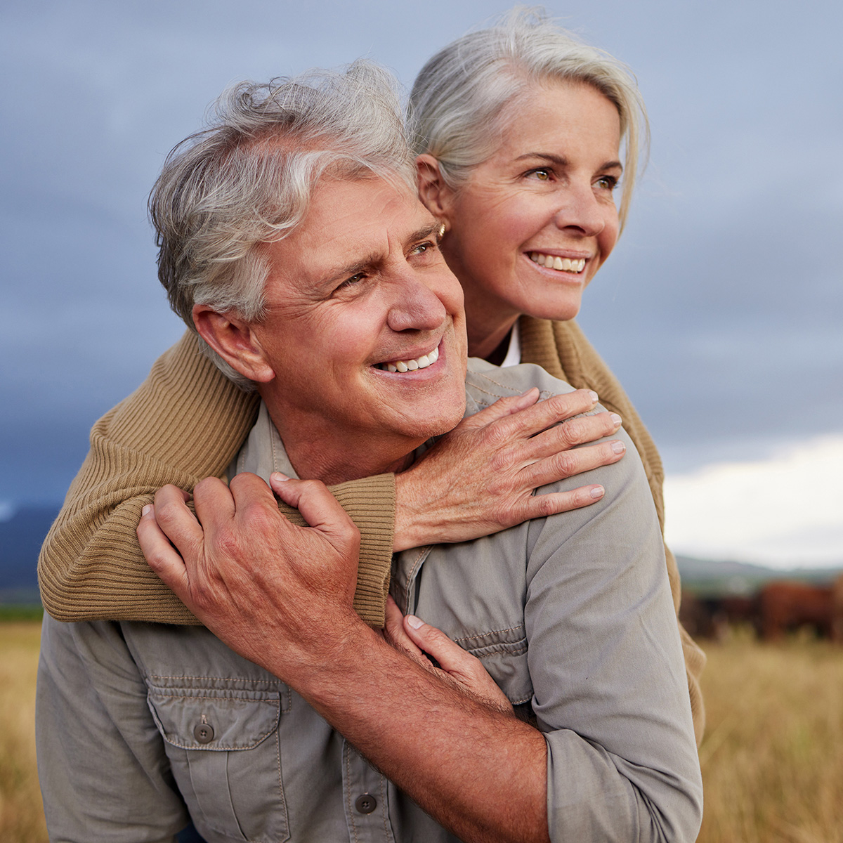 Mature couple embracing and looking happy while bonding outdoors at a farm, carefree and loving. Senior husband and wife having peaceful day in nature, enjoying retirement and relationship.